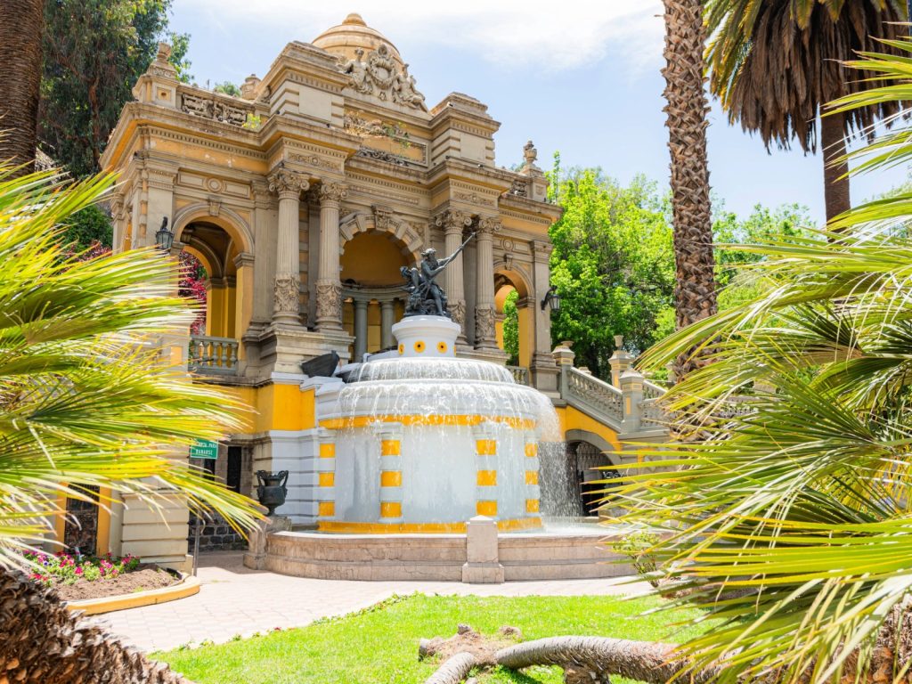 Un cerro urbano con vegetación densa, árboles y senderos peatonales. Se observan estructuras arquitectónicas antiguas de estilo clásico (escaleras de piedra, fachadas o estatuas) integradas en la naturaleza del cerro, con edificios de la ciudad visibles en la periferia.