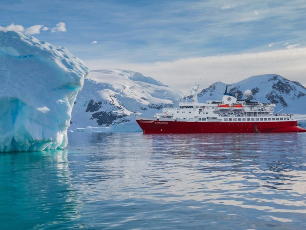 Paisaje polar dominado por el color blanco de la nieve y el hielo. Se observan grandes formaciones de hielo, glaciares o icebergs flotando en un mar oscuro. El cielo suele estar nublado o con una luz blanca difusa de alta intensidad.