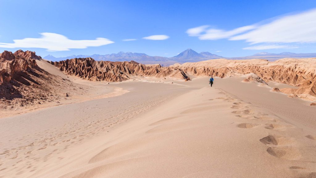Un turista avanza de frente por un sendero arenoso del Valle de la Luna, rodeados por los imponentes farallones de roca rojiza del desierto de Atacama, reflejando cómo es posible hacer amigos al viajar solo en Chile.