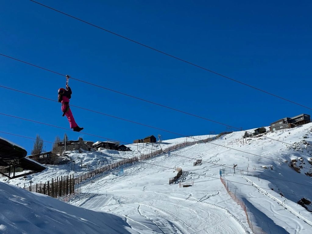 Una persona con traje rosado se desliza en canopy suspendida por cables sobre las pistas de la Cordillera de los Andes en el parque de nieve en Santiago.