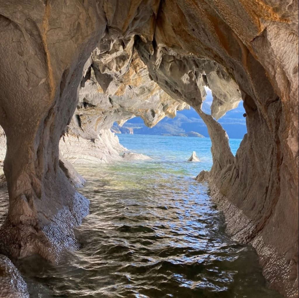 Vista desde el interior de una de las Cavernas de Mármol hacia el lago General Carrera, mostrando las paredes de roca erosionada con tonos grises y ocres que enmarcan el agua azul brillante.