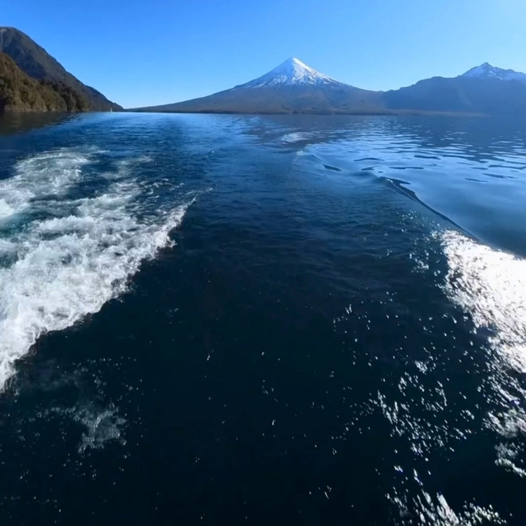 Estela de espuma dejada por una embarcación navegando por el Lago Todos los Santos, con el volcán Osorno de cima nevada elevándose al fondo, uno de los destinos secretos de Chile en el sur del país.