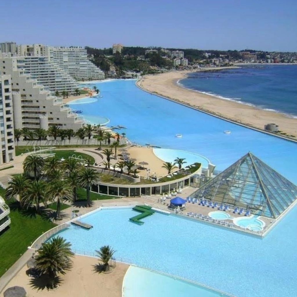 Vista aérea de la piscina de San Alfonso del Mar en Algarrobo, con sus extensas aguas turquesa, edificios residenciales, palmeras y la playa del océano Pacífico al fondo, uno de los destinos secretos de Chile más sorprendentes.