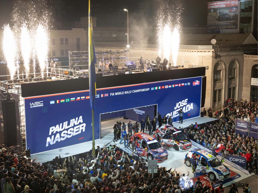 Ceremonia nocturna de partida del Rally Chile Biobío 2026 en la Plaza de la Independencia de Concepción, con autos de competencia, fuegos artificiales y una multitud de espectadores.