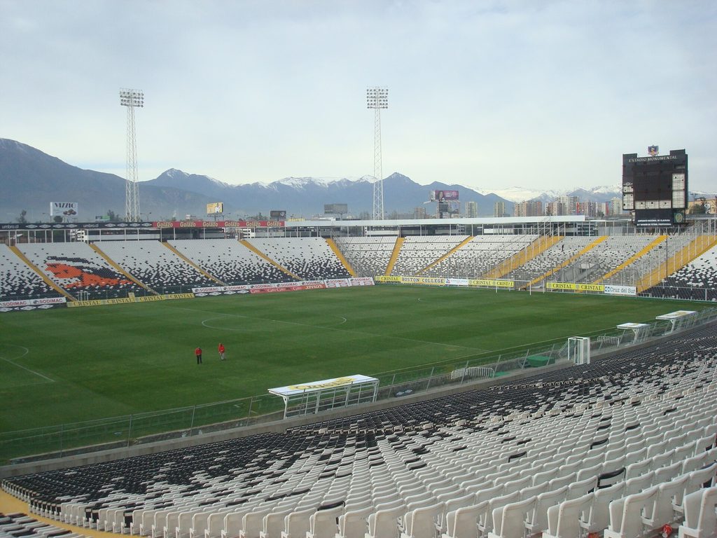 Graderías del Estadio Monumental con el mosaico del emblema de Colo-Colo formado en los asientos, publicidad de patrocinadores y la cordillera nevada de fondo.