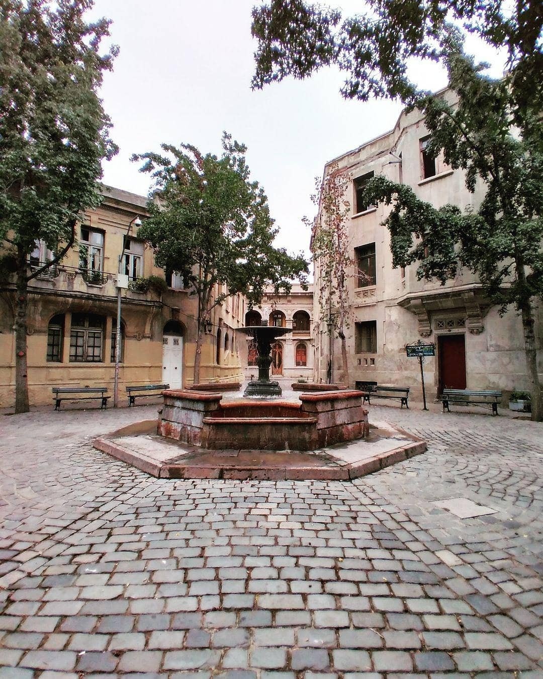 Stone fountain in the cobblestone plaza of Barrio Concha y Toro in Santiago, surrounded by trees, benches, and early 20th-century mansion facades