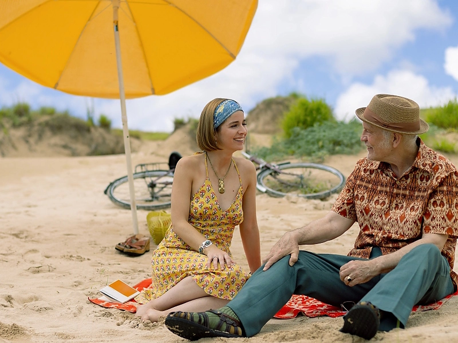 Mariana Di Girolamo und John Malkovich unterhalten sich sitzend am Strand während einer Szene aus Wild Horse Nine.