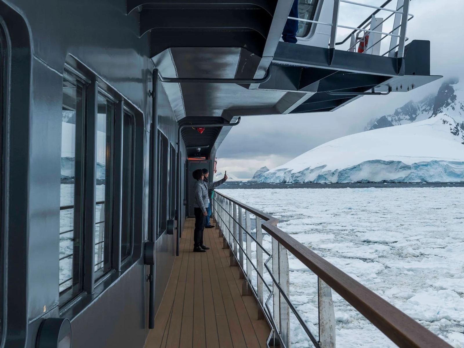 Passengers on an Antarctica cruise watching icebergs and snow-capped mountains from the ship’s deck.