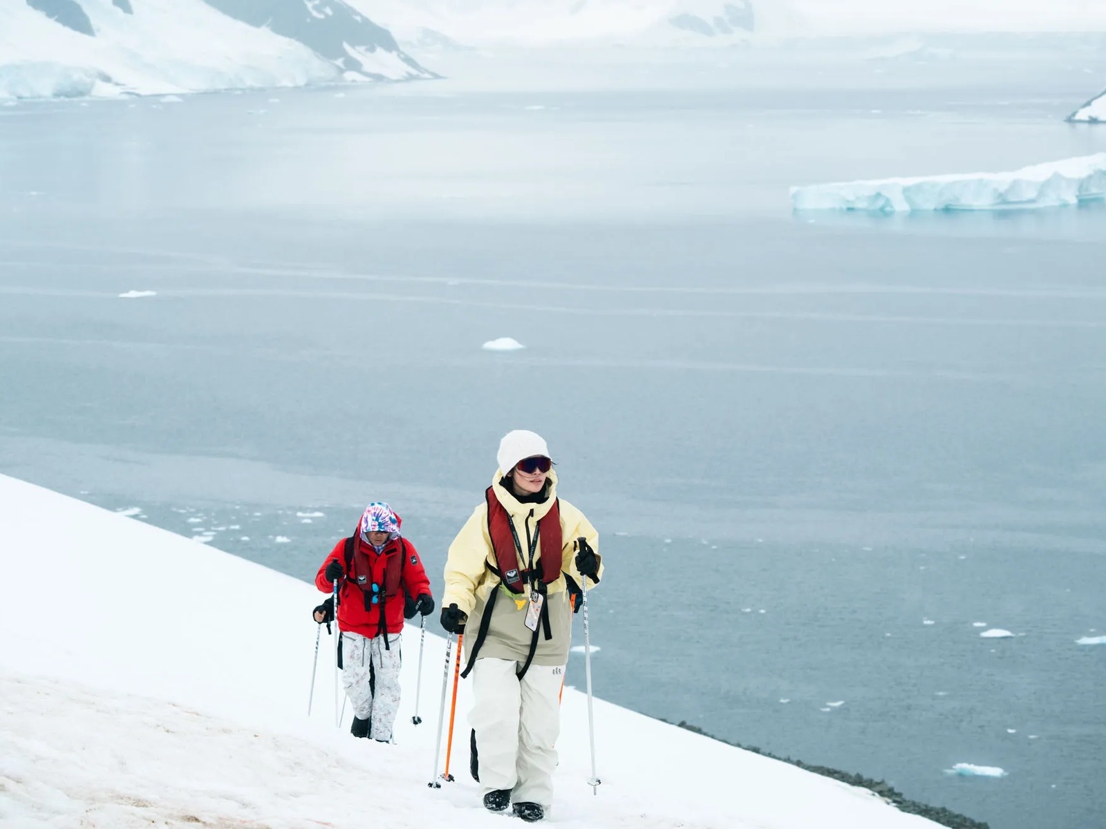 Passengers with trekking poles walking on snow by the sea during an excursion on the Antarctic Peninsula.