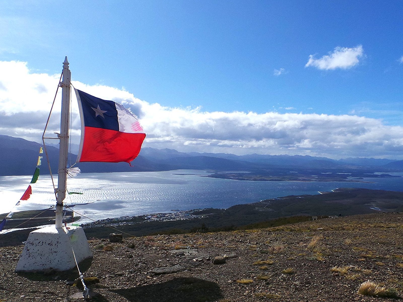 Chilean flag waving at the top of a hill overlooking a lake and mountains in Patagonia.