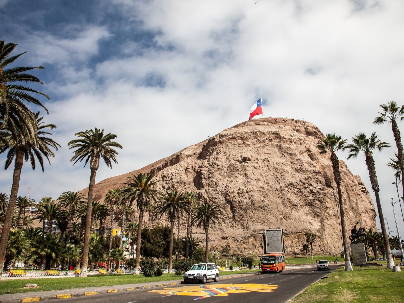 Chilean flag flying over the Morro de Arica, surrounded by palm trees, with views of the city and the Pacific Ocean.