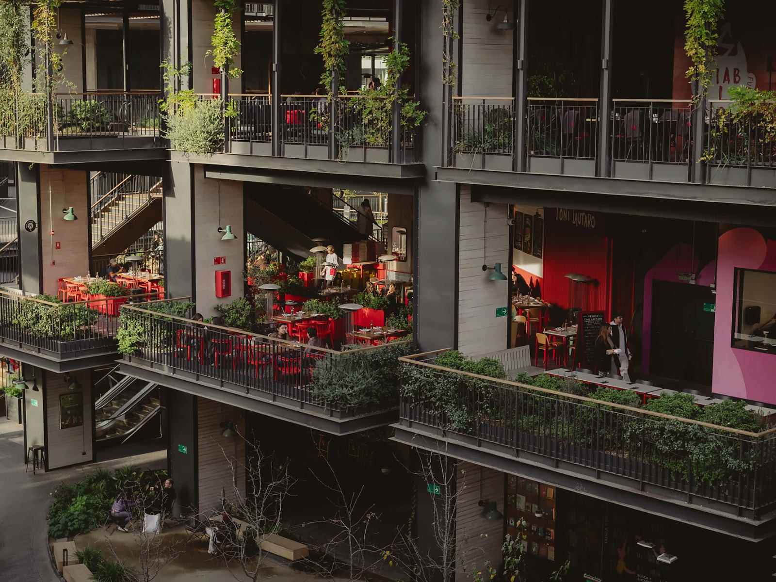 Terraços de restaurantes com cadeiras vermelhas e abundante vegetação nas varandas do MUT, um dos espaços gastronómicos de Santiago.