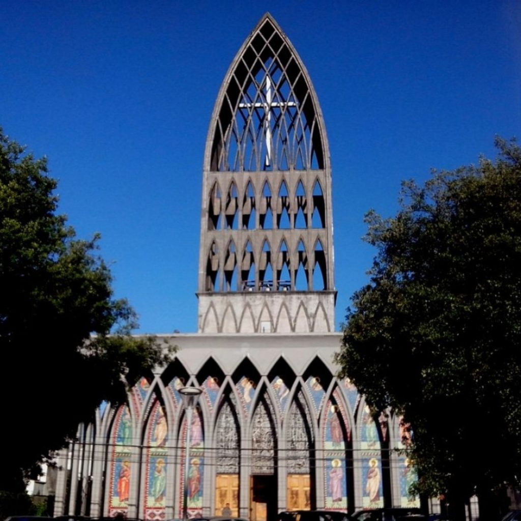 Catedral San Mateo de Osorno vista de frente con su moderna y monumental torre ojival de 45 metros coronada por una gran cruz interior. En la base destacan los arcos apuntados con coloridos mosaicos religiosos y vitrales.