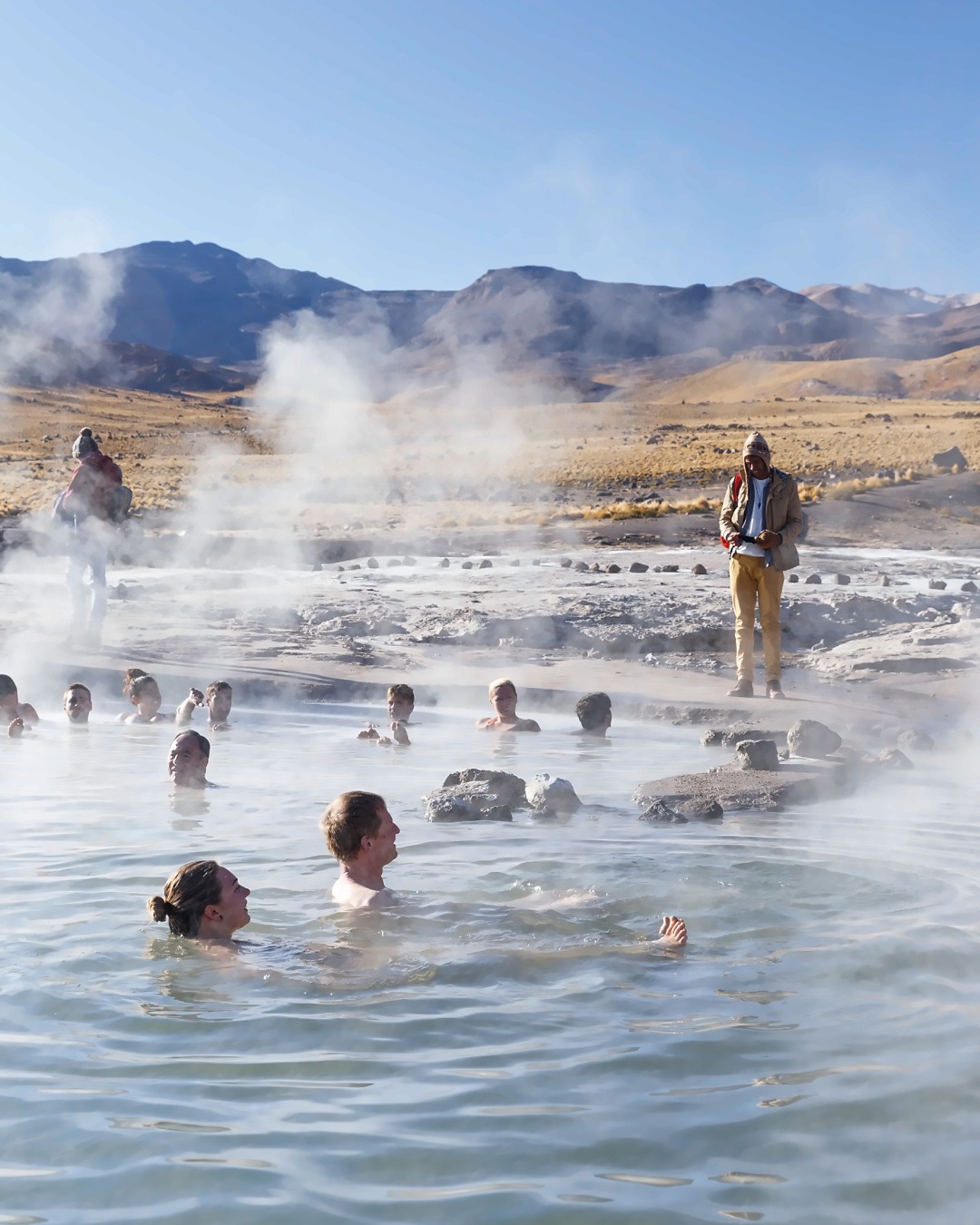 Bathers in a thermal pool surrounded by steam at El Tatio Geysers, one of the high-altitude experiences when traveling from Patagonia to the Atacama Desert.