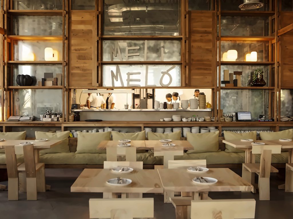 Mesas de madera clara, sillones con cojines verdes y la cocina abierta de Meli Meló, espacio all day con brunch y almuerzo, ideal si buscas dónde comer en el MUT.